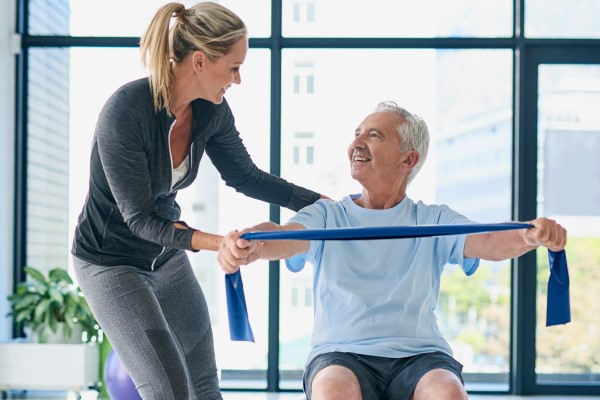 Allied health worker helping old man in gym